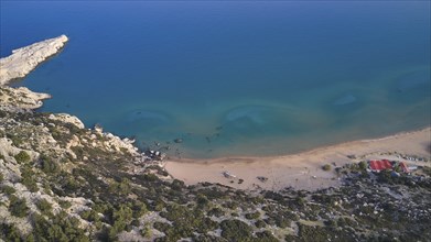 Aerial view of a secluded beach with clear water and small huts on the shore, Tsambika Beach,