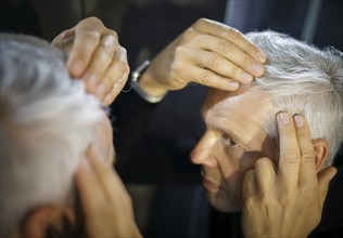 Symbolic photo on the subject of a high hairline and receding hairline. A man looks at his hairline