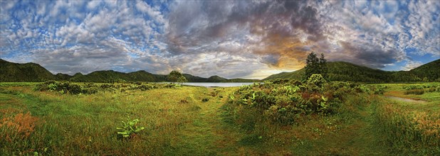 360° panorama with a meadow and mountains in the background, a lake in the distance, dramatic sky