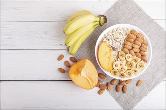 A plate with muesli, almonds, banana, sliced persimmon on a white wooden background. top view. copy