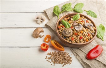 Spelt (dinkel wheat) porridge with vegetables and mushrooms in wooden bowl on a white wooden