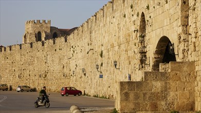 Old city wall next to a road with passing scooter in sunshine, harbour area, Rhodes Town, Rhodes,