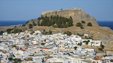 Whitewashed houses of a mountain village under an old fortress on a sunny day, Acropolis of Lindos,