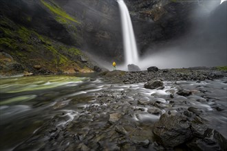 Young man with yellow jacket standing in front of waterfall, Haifoss and Granni waterfall at a