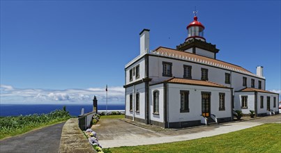 A white lighthouse with red roofs and a display by the sea under a clear blue sky, Farol da