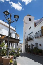 Picturesque Spanish street with whitewashed buildings, a church tower and lush plants in the