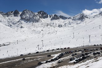 Schneebedecktes Skigebiet in den Bergen mit Skiliften und Autos auf dem Parkplatz unter einem