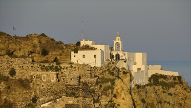 A castle and white buildings on a cliff, illuminated by the golden light of dawn with the sea in