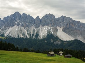 Alpine huts in front of the Geisler peaks under a cloudy sky, Villnöss Valley, Sass Rigais,