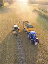 Aerial view of a tractor and a harvester collecting hay in a field at sunset, Haselstaller Hof,