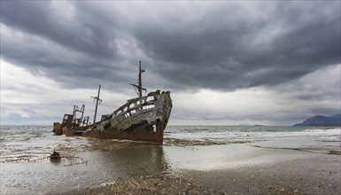 An abandoned, rusty shipwreck lies on the shore under an ominously cloudy sky, symbol photo, AI