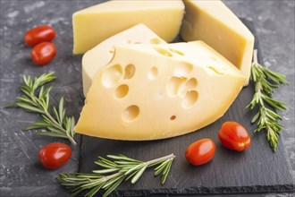 Various types of cheese with rosemary and tomatoes on black slate board on a black concrete