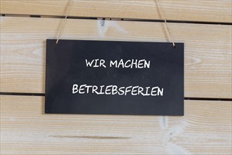 Symbolbild für Betriebsferien: Schild auf einer Holztafel mit der deutschen Aufschrift WIR MACHEN