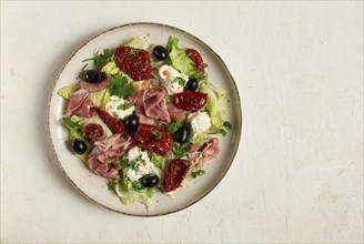 Salad with dried tomatoes, prosciutto, soft cheese, olives, homemade, top view