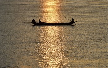 Fisherman paddle down the Brahmaputra river to sell their catch at a market during sunset, in