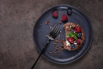 Half-eaten chocolate tartlet, on a plate, stuffed with cottage cheese and berries, breakfast,