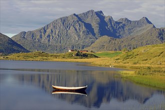 A small wooden boat floats on a calm lake with majestic mountains in the background, Leknes,