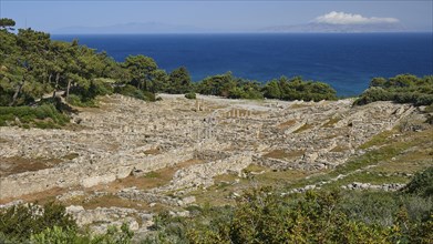 Ruins of an ancient site in front of a blue sea and tree-lined terrain, Kamiros, Archaeological