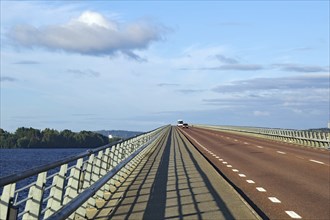 Long bridge over water with blue sky and few clouds, shadow on road, Storsjon, Fröson Bridge,