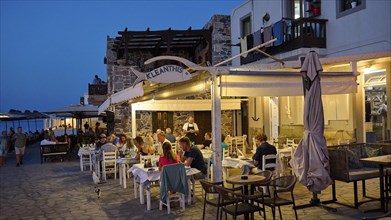 A restaurant on the street where people eat and chat by candlelight at dusk, Mandraki, Nisyros,