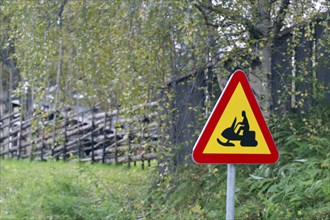 Red and yellow warning sign for tobogganing on a grassy hill in a natural environment with trees,