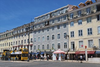 Lively street with many shops and tall buildings, people and a bus under a sunny sky, house with