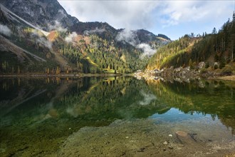 The Vordere Gosausee in autumn with a view of the Gasthof Gosausee. Sun and clouds. Reflection.