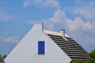 White cottage with thatched roof and round window under a blue sky, Saintes-Maries-de-la-Mer,