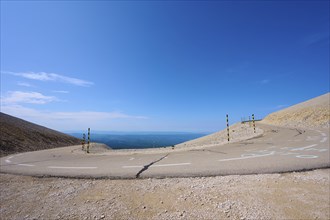 An empty mountain road with a hairpin bend under a clear blue sky and barren landscape, Mont