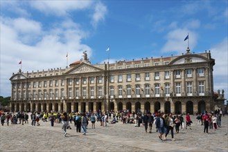 A large baroque stone structure with many windows and visitors in front of it in an open square