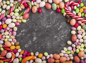 Colorful frame of multicolored candies on a black concrete background. Christmas cane, chocolate