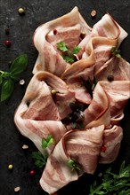 Raw bacon, sliced, with micro greenery and spices, on a black background, close-up