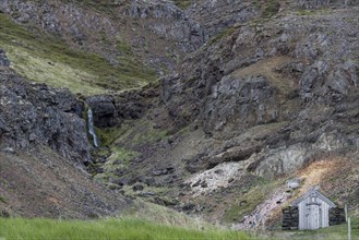 Old hut with stone walls and grass roof, waterfall, Laugar, Westfjords, Iceland, Europe