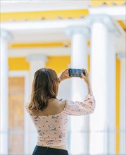 Young tourist taking photos of a tourist cathedral with cell phone. Girl taking photos of the