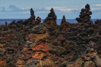 Several layered piles of lava rocks in a barren landscape with the ocean in the background, A Porta