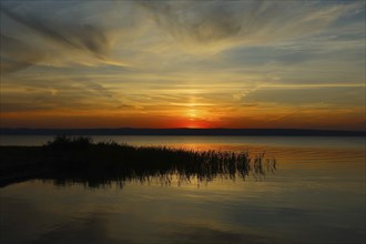 Dramatic sunset at Lake Neusiedl in Austria with colourful orange and red illuminated cloudy sky,