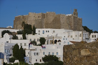 Hill with a castle and traditional white houses surrounded by trees and vegetation under a clear