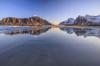 Snow-covered mountains reflected in water on the beach, sea, morning light, winter, Flakstadoya,