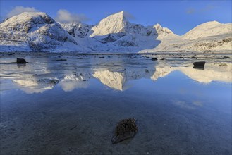 Snow-covered steep mountains reflected in fjord, morning light, winter, Flakstadoya, Lofoten,