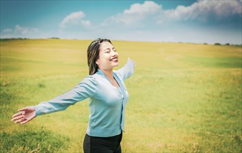 Serene young woman breathing fresh air in beautiful field spreading arms. Happy girl spreading arms