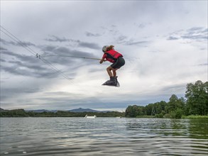 Boy or girl flies over the lake, jump with wakeboard, red life jacket, water skiing in wakepark,