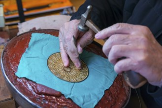 Close-up of hands engraving a detailed pattern on a metal plate in an artisanal process, Toledo,