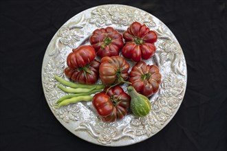 Tomatoes, ox hearts and a Vorgebirgstrauben pickled cucumber on a decorative plate on a black