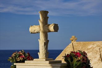 A stone cross and flowers against a clear blue sky, Agios Nikolaos church, cemetery, Pigadia, town