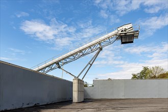 Large conveyor belt towers over a wall, contrasting with blue sky