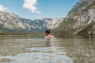 Woman standing in clear water with mountain landscape in the background, Soca Valley, Slovenia,