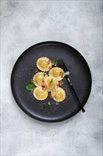 Fresh ravioli, with butter, spices and herbs, fried bacon, on a black plate, top view, dark