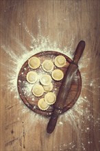 Fresh raw, uncooked ravioli, on a cutting board, with a rolling pin for dough, wooden background,