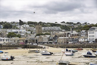 Beach with boats at low tide, view of town building and church under cloudy sky, town of St Ives in