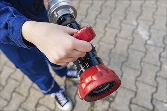 Child holding a fire hose with red handles on a cobbled floor, fire brigade, Enzklösterle, Black